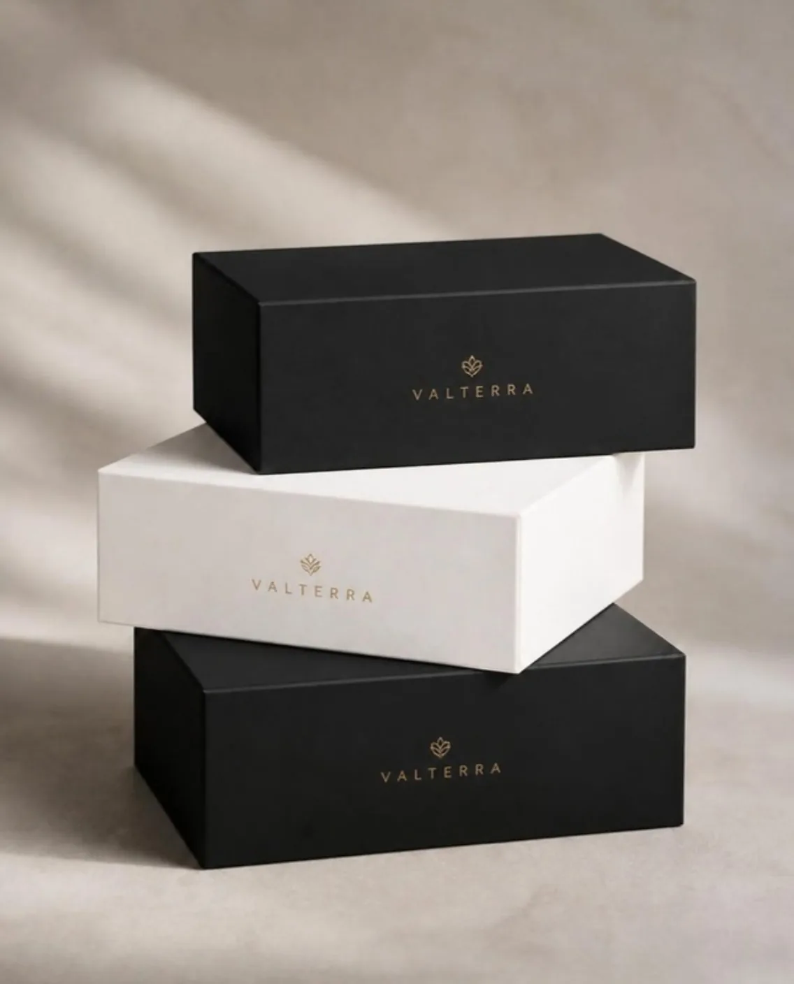 Gestapelte Geschenkboxen in Schwarz und Weiß mit Logo in Goldfolie