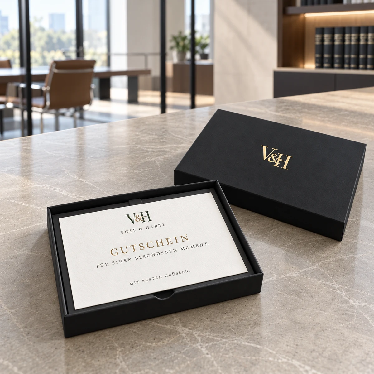 Schwarze Stülpdeckelbox mit Gutscheinkarte, daneben der Deckel mit Monogramm in Goldfolie
